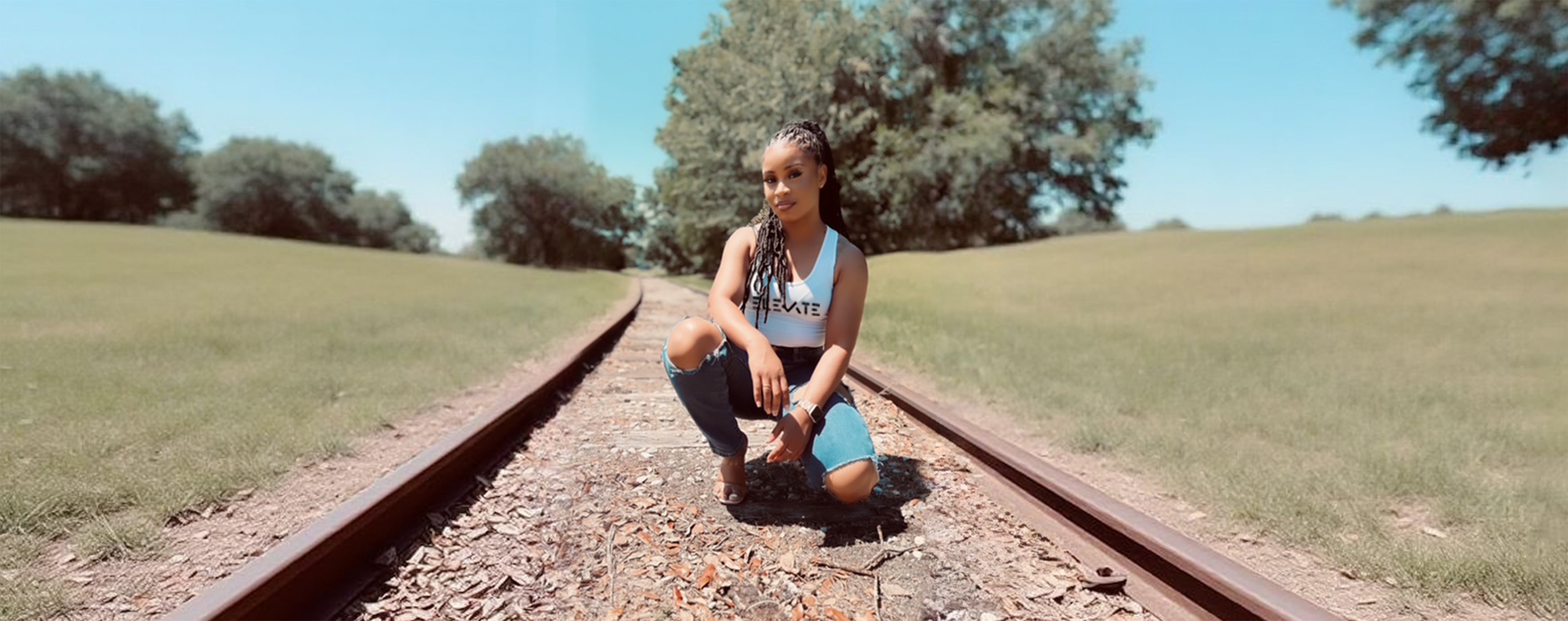 Person sitting on a railway track in a grassy field with trees in the background
